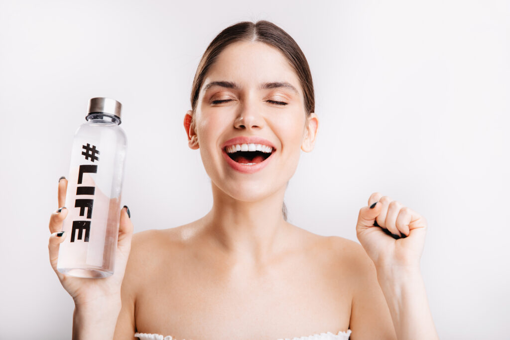 portrait of pleased lady without makeup, posing with pleasure in great mood with bottle of water on isolated background.