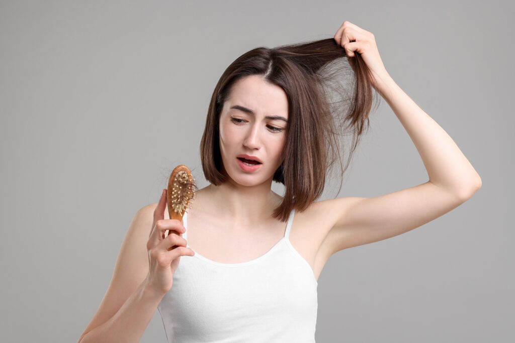 sad woman holding brush with lost hair on grey background. alope